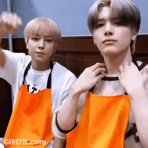 Two Young Men Wearing Orange Aprons Are Posing For A Picture Together . GIF