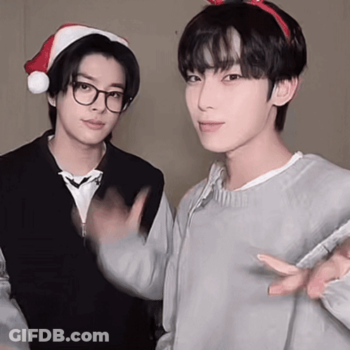 Two Young Men Wearing Santa Hats Are Standing Next To Each Other . GIF