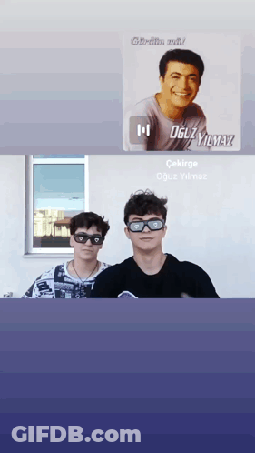 Two Young Men Wearing Sunglasses Are Standing Next To Each Other In Front Of A Window With A Picture Of Oguzyilmaz In Th GIF