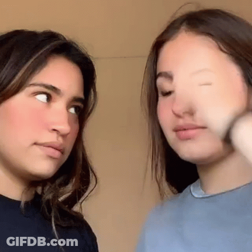 Two Young Women Are Standing Next To Each Other And Looking At Each Other With Their Eyes Closed . GIF