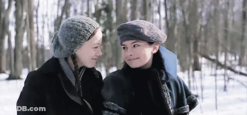 Two Young Women Are Standing Next To Each Other In The Snow And Looking At Each Other . GIF