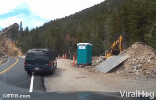 Van Driving Down Road Beside Portable Toilet And Bulldozer GIF