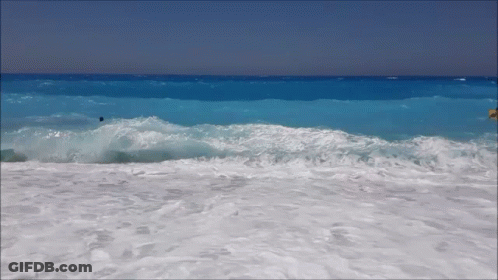 Waves Crashing Against A Sandy Beach With A Person In The Water GIF