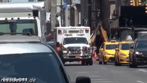 White Ambulance Driving Down Busy Street Next To Taxis GIF