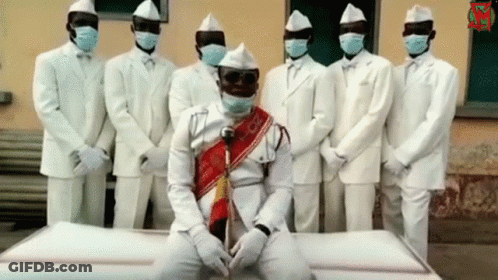 White Suited Men With Masks Around White Coffin GIF