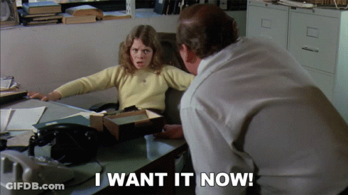 Woman At Desk With Man Behind Saying I Want It Now GIF