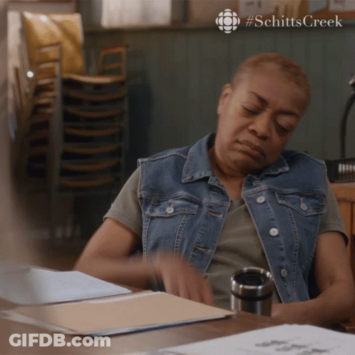 Woman At Desk With Stack Of Chairs Schitts Creek GIF