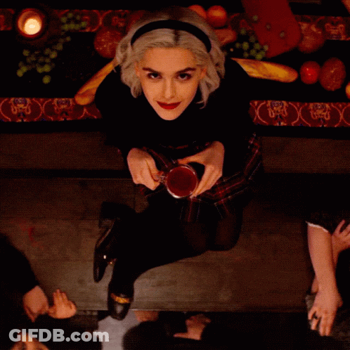 Woman At Table Holding Glass Of Red Liquid GIF