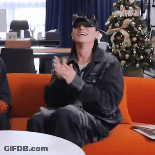 Woman Clapping On Orange Couch By Christmas Tree GIF