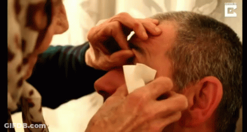 Woman Cleaning Man's Eye With Paper GIF