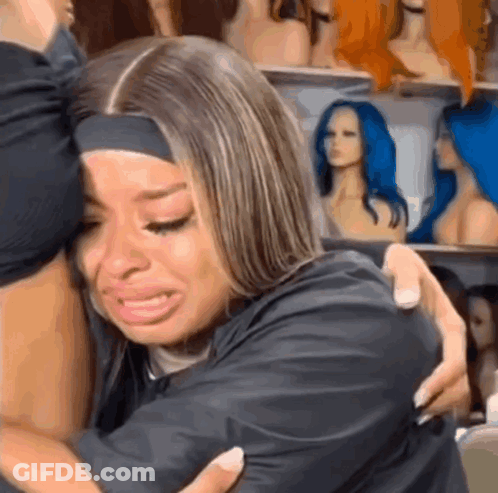 Woman Crying Hugging Another Woman In Front Of Wigs GIF