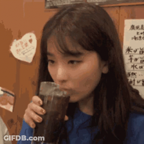 Woman Drinking Soda By Wall With Chinese Writing GIF