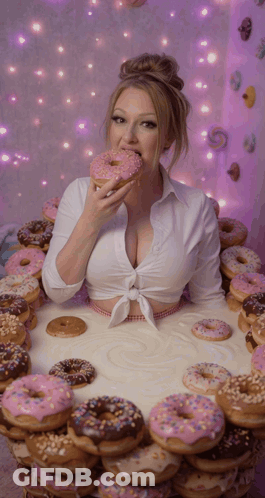 Woman Eating Donut In Front Of Table Full Of Donuts GIF