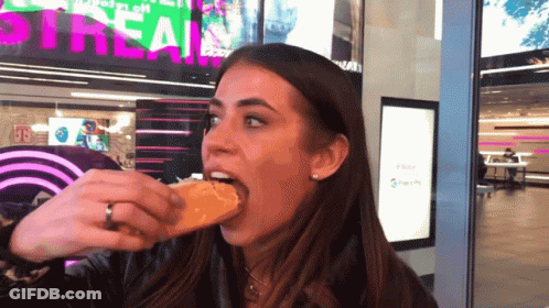 Woman Eating Sandwich In Front Of Stream Sign GIF