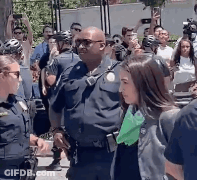 Woman Escorted By Police Officer As Crowd Takes Pictures GIF