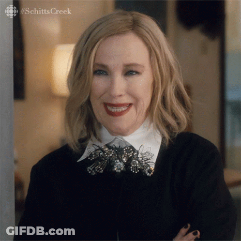Woman From Schitts Creek Smiling In Black Jacket And White Collar GIF