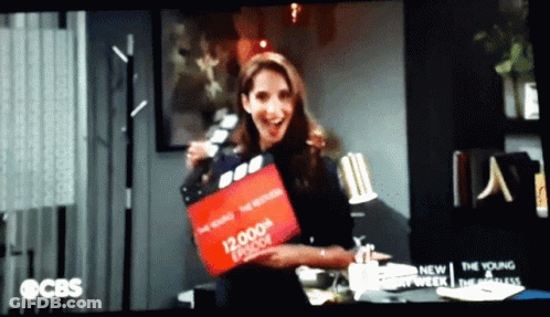 Woman Holding 12,000Th Episode Clapper Board GIF