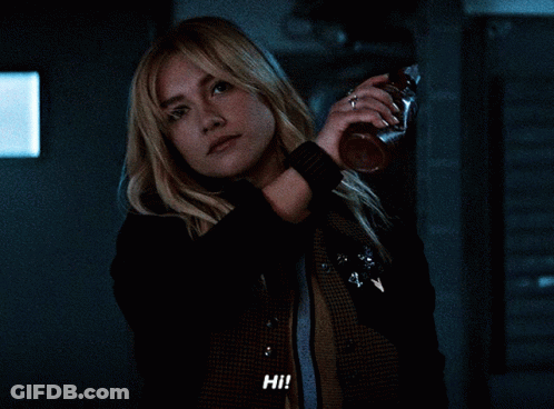 Woman Holding Bottle Saying Hi In Dark Room GIF