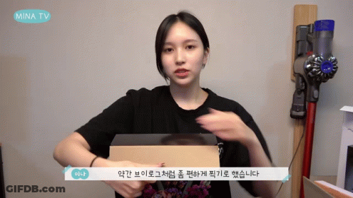 Woman Holding Box In Front Of Mina TV Sign GIF