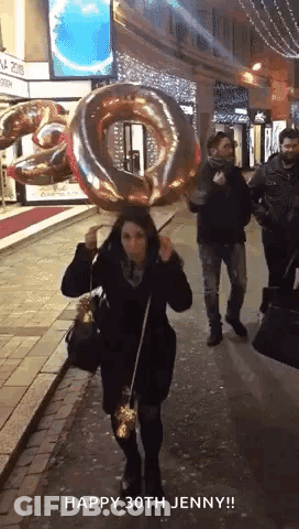 Woman Holding Number 30 Balloon On Head Walking Down Street GIF