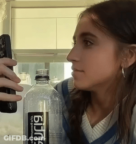 Woman Holding Remote Next To Bottle Of Bjing GIF