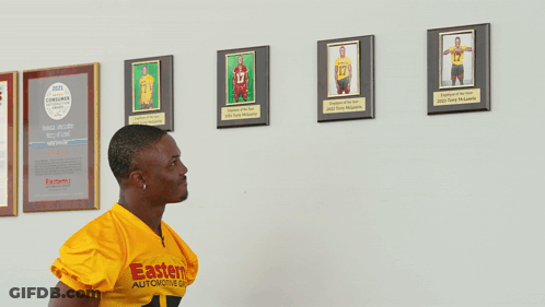 Woman Holding Shirt With Man's Picture While Basketball Player Sits GIF