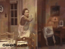 Woman In Apron Standing In Room With Table And Chairs GIF