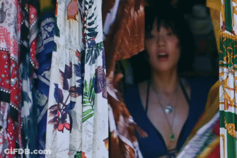 Woman In Bikini In Front Of Colorful Clothes GIF