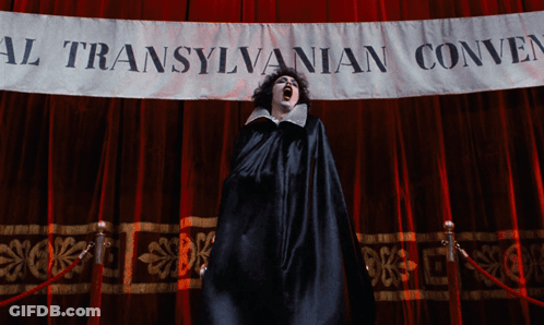 Woman In Black Cape In Front Of Transylvanian Convention Banner GIF