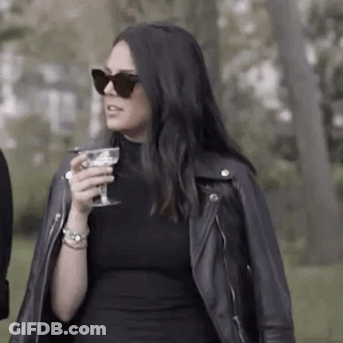 Woman In Black Dress And Leather Jacket Holding Wine GIF