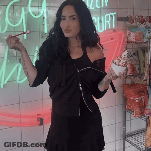 Woman In Black Dress Holding Ice Cream In Front Of Yogurt Sign GIF