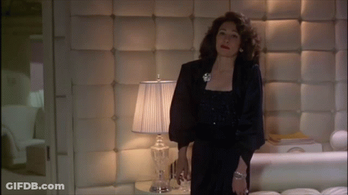Woman In Black Dress In Front Of Lamp In Bedroom GIF