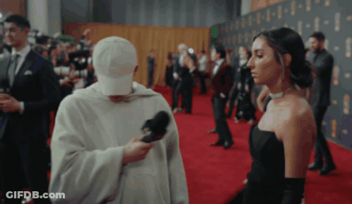 Woman In Black Dress Interviewed By Man In White Hat On Red Carpet GIF