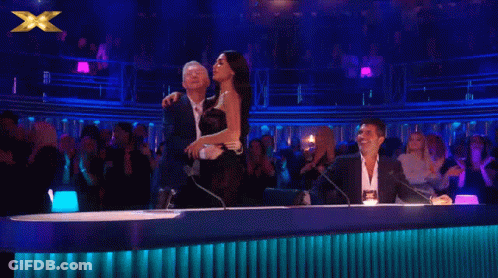 Woman In Black Dress Next To Man And Man In Suit Behind Microphone GIF