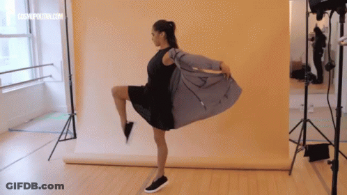 Woman In Black Dress On One Leg Yellow Wall GIF