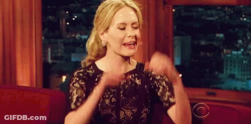 Woman In Black Dress On Red Couch With Arms In Air GIF
