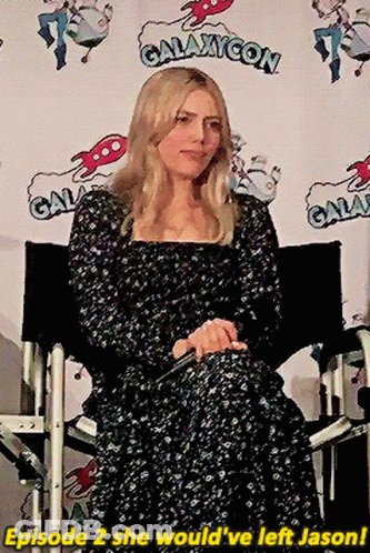 Woman In Black Dress Sitting In Front Of Galaxycon Sign GIF
