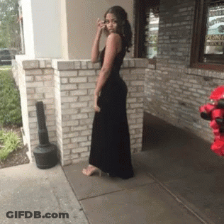 Woman In Black Dress Standing In Front Of Brick Building GIF