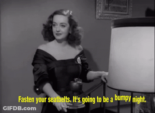 Woman In Black Dress Standing Next To Lamp Says Fasten Your Seatbelts GIF