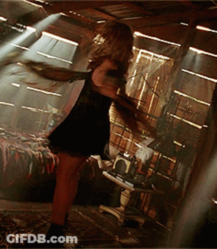 Woman In Black Dress With Arms Outstretched In Dark Room GIF