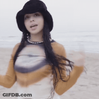 Woman In Black Hat And Yellow Shirt Standing On Beach GIF