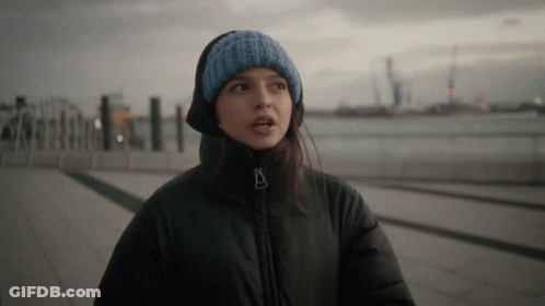 Woman In Black Jacket And Blue Knitted Hat Looking At Camera GIF