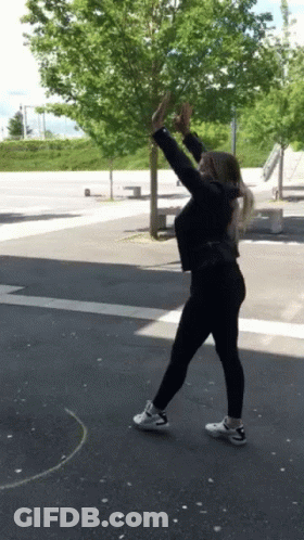 Woman In Black Jacket Arms In Air On Street GIF