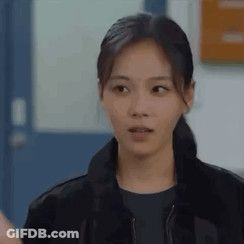 Woman In Black Jacket Standing In Front Of Door Looking At Camera GIF