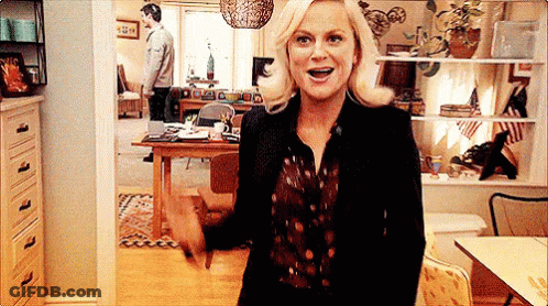 Woman In Black Jacket Standing In Living Room With Man In Background GIF