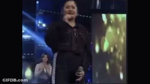 Woman In Black Jumpsuit Holding Microphone On Stage GIF