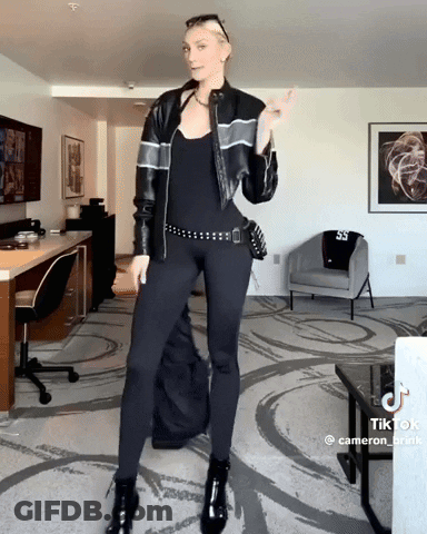 Woman In Black Leather Jacket And Leggings Standing In Living Room GIF