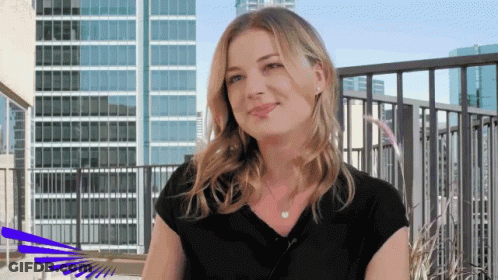 Woman In Black Shirt On Balcony In Front Of Tall Buildings GIF