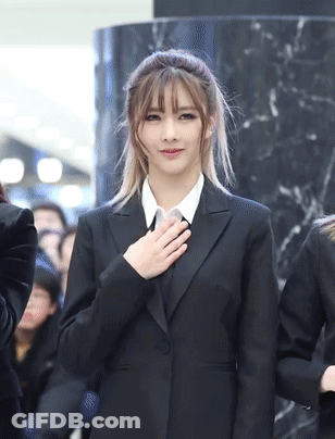 Woman In Black Suit Holding Hand To Heart GIF