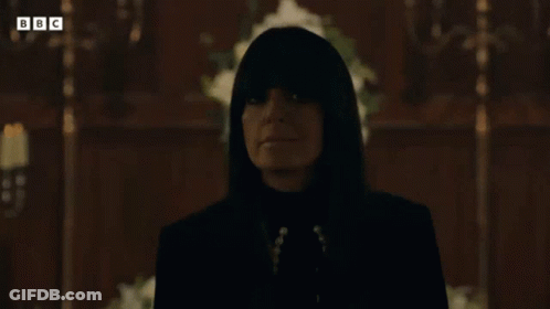 Woman In Black Suit Standing Before Cross In Dark Room GIF